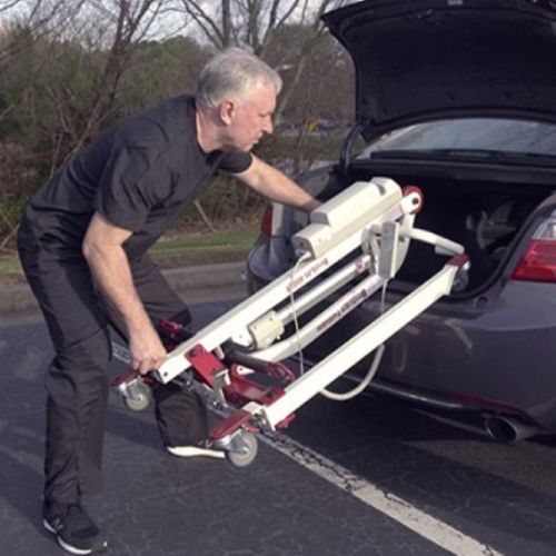 Lift shown being placed into the truck of a car due to the lifts easily collapsable features 