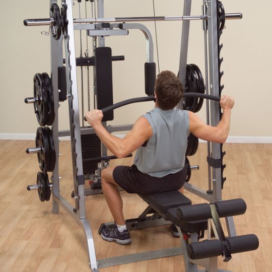 The user is strengthening his arm, shoulder, and upper back muscles with the pull down weight bar of the Body-Solid Series 7 Smith Gym System.