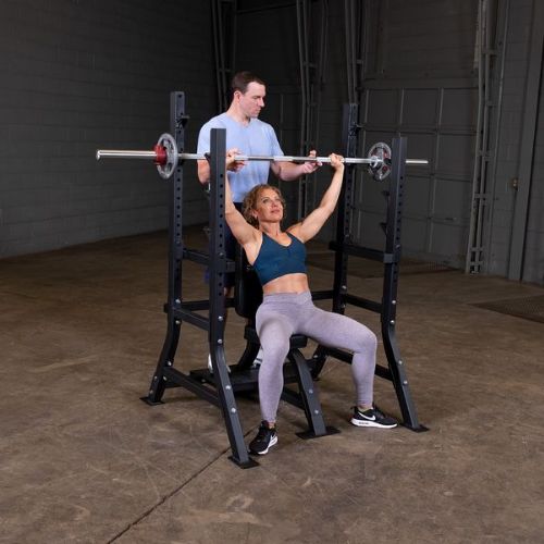 Executing shoulder press with spotter on the foot plate (barbell and weights not included)