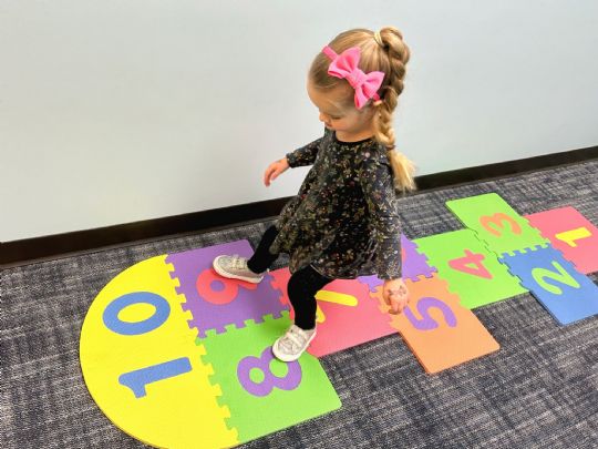 Young girl playing hopscotch on colorful foam number tiles, promoting active learning and fun