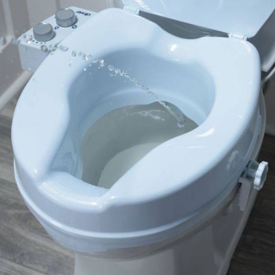 Bidet spray feature on raised toilet seat for enhanced personal hygiene