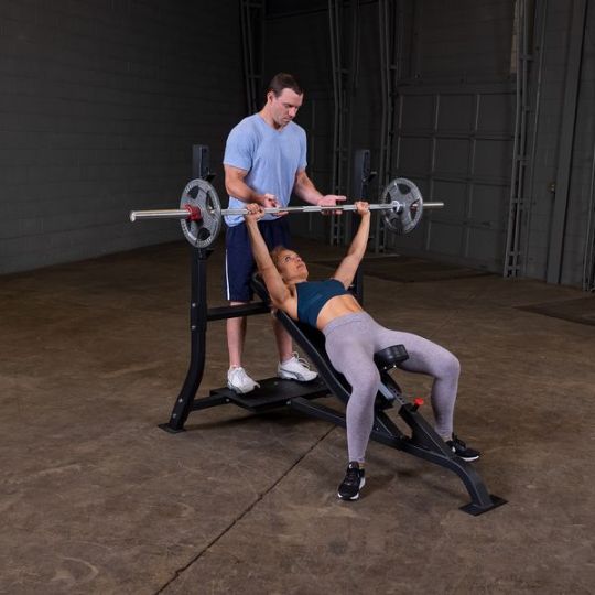 Executing incline barbell press with spotter (barbell and weights not included)