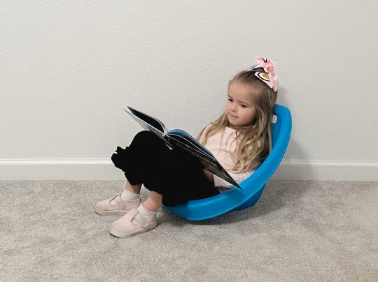 Young girl comfortably reading in a blue kore scoop rocker chair