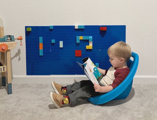 Young boy sitting in a blue kore scoop rocker chair reading a book