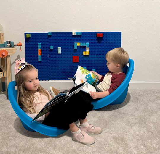 Two young children reading books in blue kore scoop rocker chairs